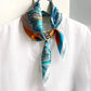 Leather scarf ring clip holding an orange and blue mulberry silk neck scarf on a hanger with a white shirt.