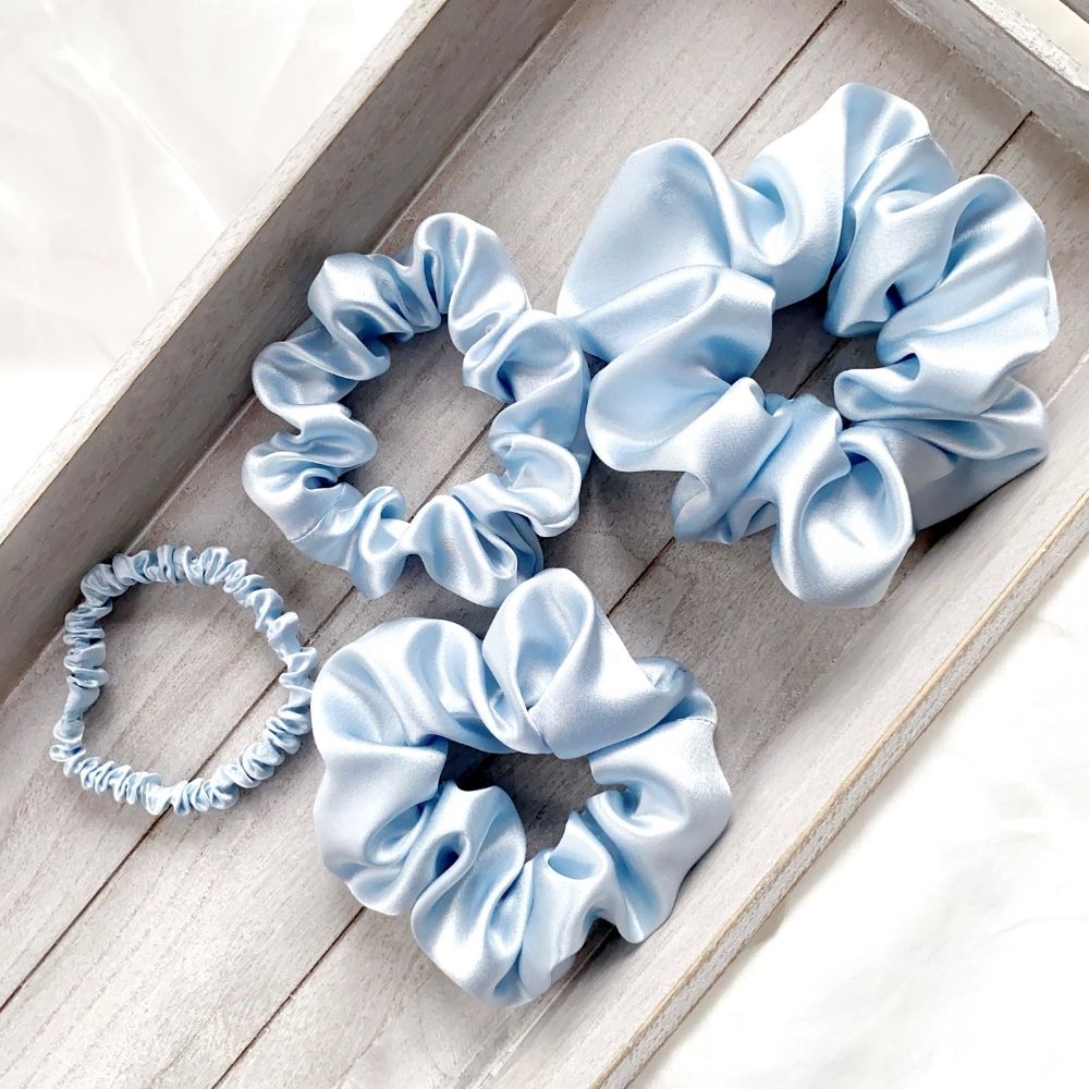 Set of light blue pure mulberry silk scrunchies and hair ties on a wooden surface