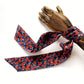 Floral  liberty silk skinny scarf with red and blue pattern draped over a wooden hand on a white background