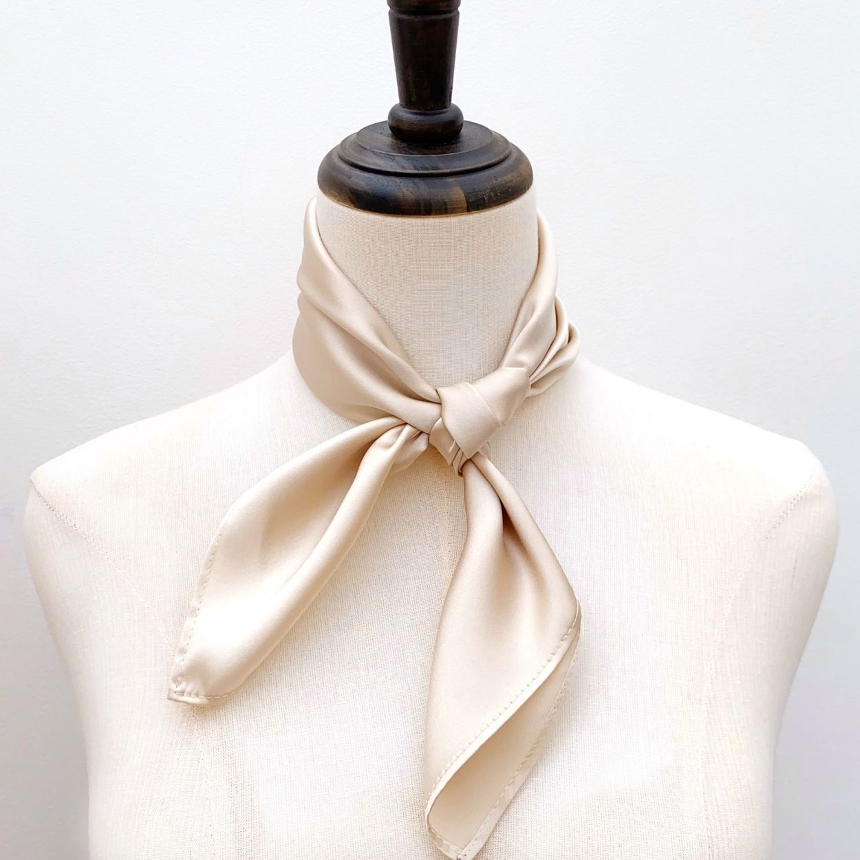 A ivory cream-colored mulberry silk square scarf tied neatly around a mannequin's neck, set against a plain white background.