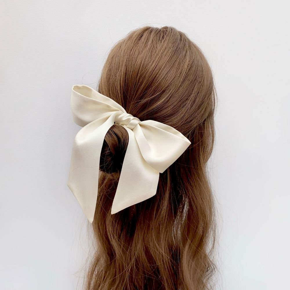 An ivory mulberry silk satin skinny hair bow accessory shown tied around the back of a woman's brown hair 