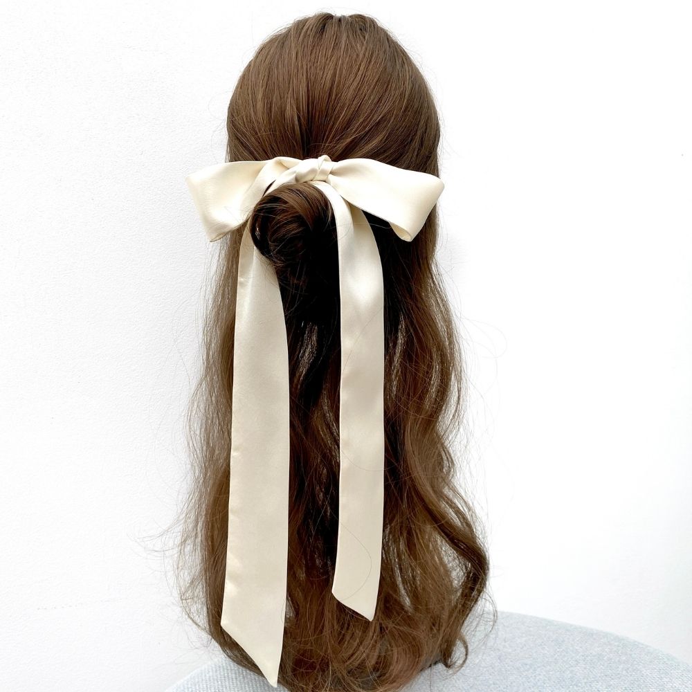 A long ivory cream skinny silk satin scarf styled in a half-up bun on a mannequin head