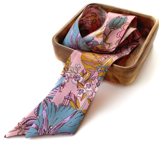 Pink liberty print silk skinny scarf in a wooden container on a white background