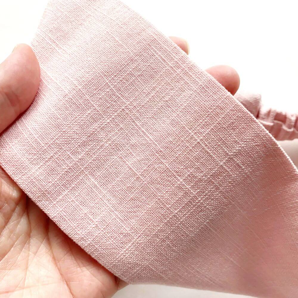 Close-up of a hand holding a pink linen headband.