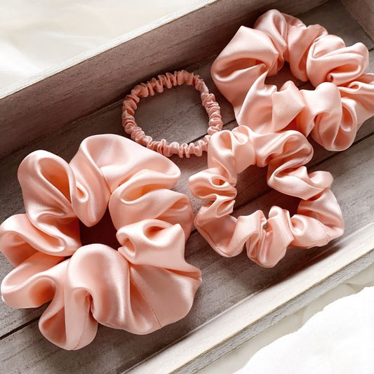 Set of pink mulberry silk satin scrunchies and silk hair ties on a wooden surface