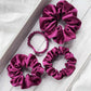 Set of four purple silk satin hair scrunchies on a light wooden surface
