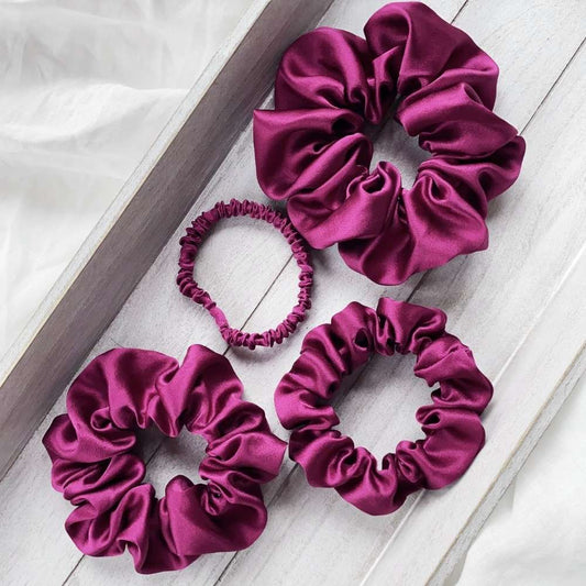 Set of four purple silk satin hair scrunchies on a light wooden surface