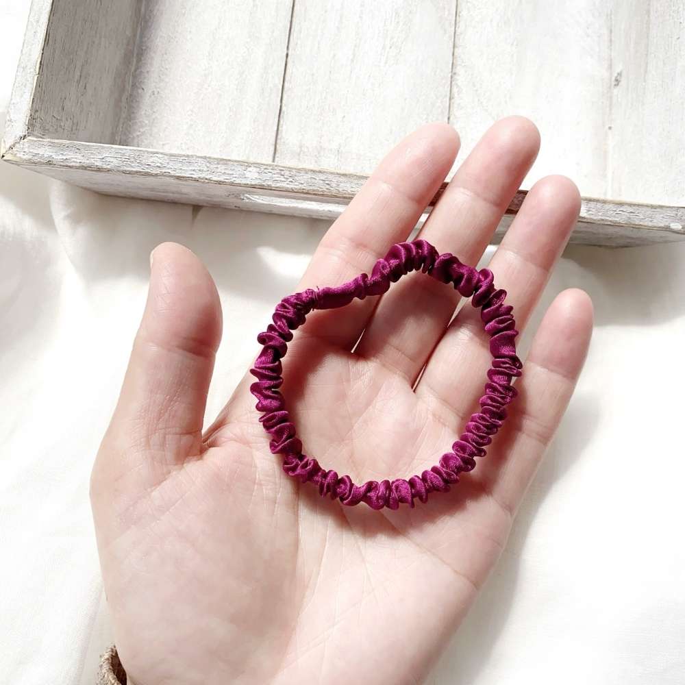 Hand holding a purple silk satin hair tie  with a light wooden box in the background