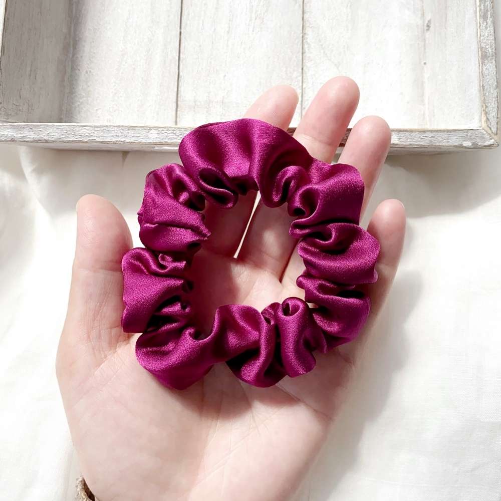 Hand holding a purple silk satin hair scrunchie against a light background