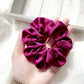 Hand holding a purple silk satin hair scrunchie against a light background