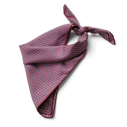 A deep red geometric and paisley print mulberry silk square scarf tied into a triangle, placed on a white background