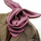 A patterned mulberry silk square scarf in red, blue, and white, tied around the collar of a brown tweed jacket against a plain white background