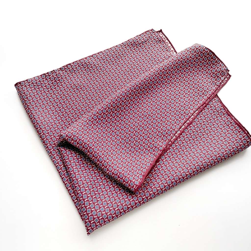 A deep red geometric and paisley print mulberry silk square scarf folded and laid flat on a white background