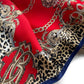 A close-up of a patterned mulberry silk square scarf featuring a bold red background with gold baroque scrollwork, leopard print sections, chain motifs, and a navy blue border.