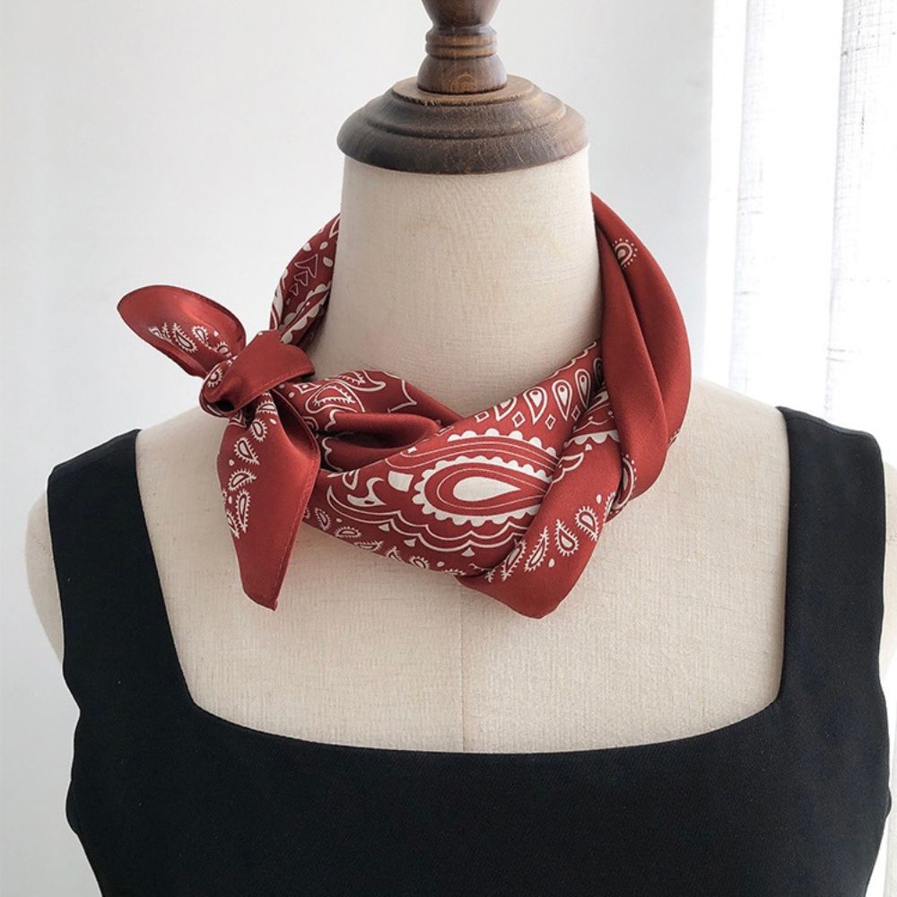 Red mulberry silk square scarf with white paisley patterns tied into a neckerchief over a mannequin's neck.
