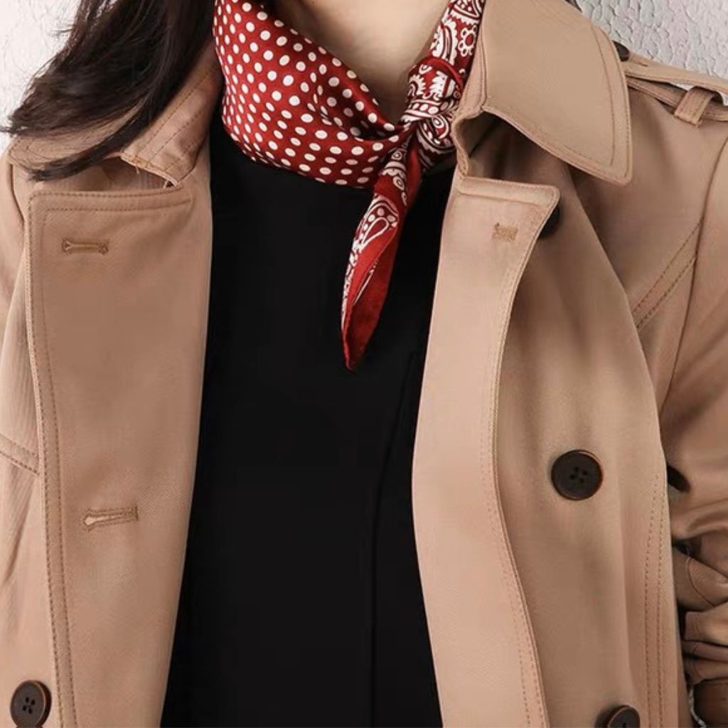 Woman wearing a khaki trench coat and black top with a red polka dot and paisley mulberry silk scarf tied around her neck.