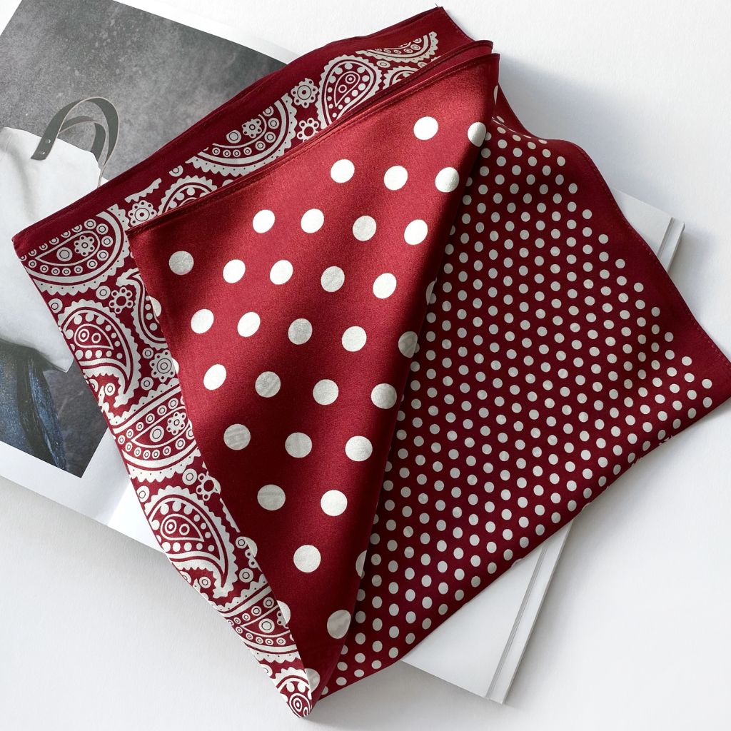 Folded rich red mulberry silk scarf with white polka dots and paisley print displayed on a magazine against a white background.