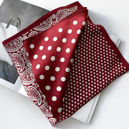 Folded rich red mulberry silk scarf with white polka dots and paisley print displayed on a magazine against a white background.