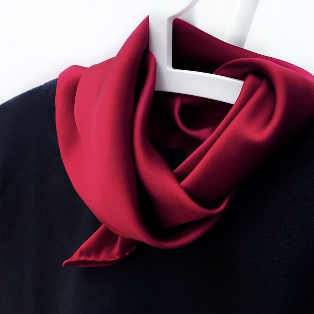 Berry red silk satin scarf tied neatly around a black top on a hanger