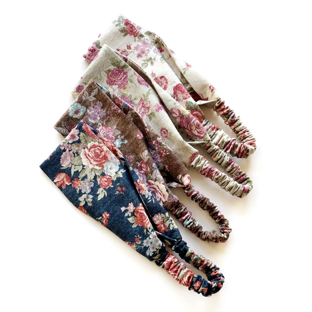 Four cotton linen fabric headbands with rose floral patterns in various colors, arranged diagonally on a plain white background.