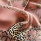 A close-up of a dusty rose mulberry silk scarf featuring a leopard print panel, ornate gold chain motifs, and baroque scrollwork.
