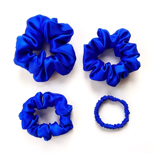 Four royal blue mulberry silk satin scrunchies and silk hair ties of different sizes on a white background