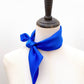 A bright royal blue mulberry silk scarf tied around a mannequin neck, set against a plain white background.