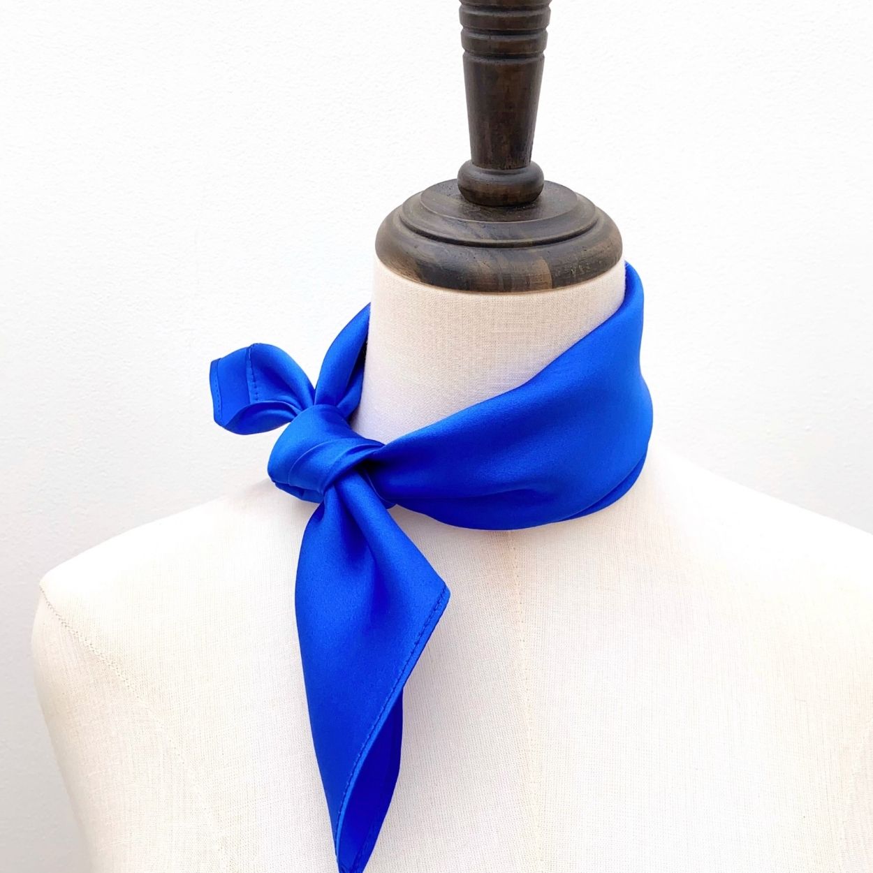 A bright royal blue mulberry silk scarf tied around a mannequin neck, set against a plain white background.
