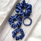 Set of four navy blue silk scrunchies on a light wooden surface.