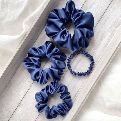 Set of four navy blue mulberry silk scrunchies on a light wooden surface.