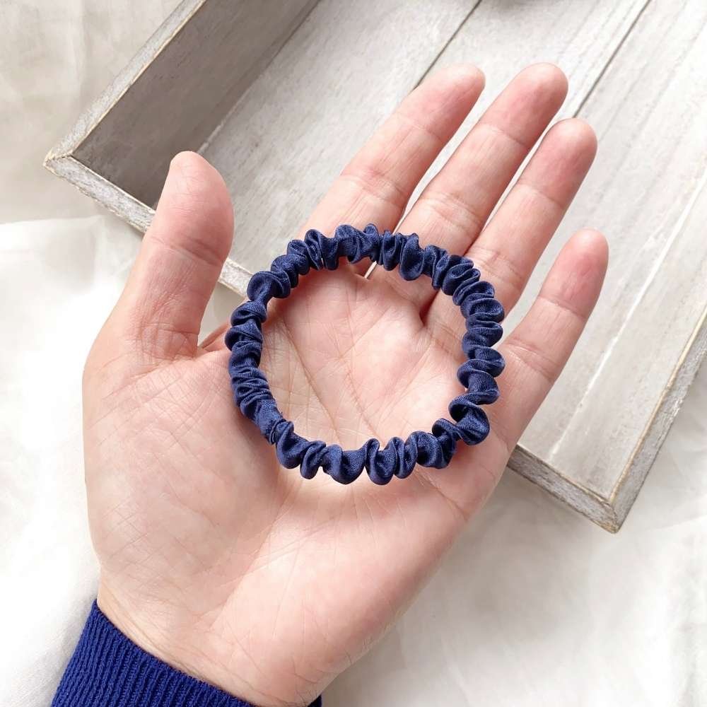 Navy blue silk hair tie held in a hand on a light wooden surface