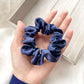 Navy blue silk scrunchie held in a hand on a light wooden surface