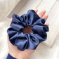 Navy blue silk satin scrunchie held in a hand against a light background