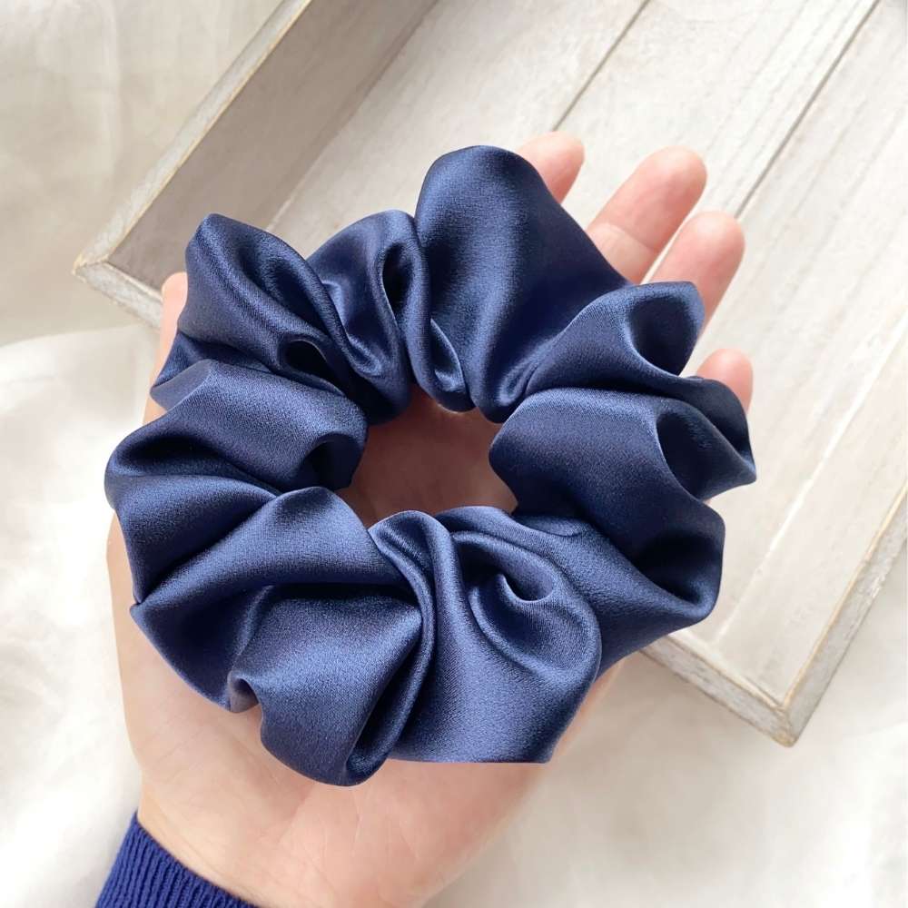 Navy blue silk satin scrunchie held in a hand against a light background