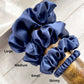 Set of blue silk hair scrunchies labeled with size on a wooden surface
