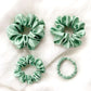 Four green silk scrunchies on a light background