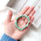 Hand holding a green silk hair tie with a wooden box in the background
