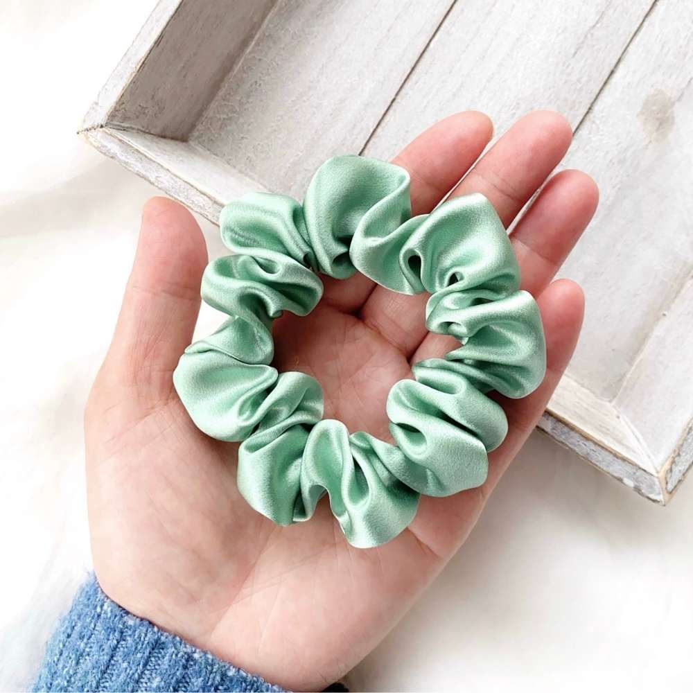 Light green silk scrunchie held in a hand with a wooden box in the background