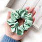 Light green silk scrunchie held in a hand on a light wooden surface