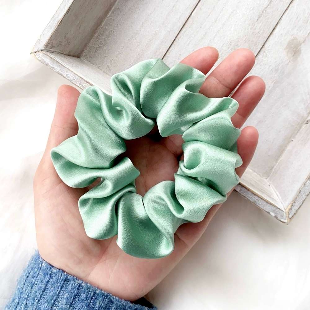 Light green silk scrunchie held in a hand on a light wooden surface