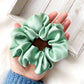 Light green silk scrunchie held in a hand on a light wooden surface