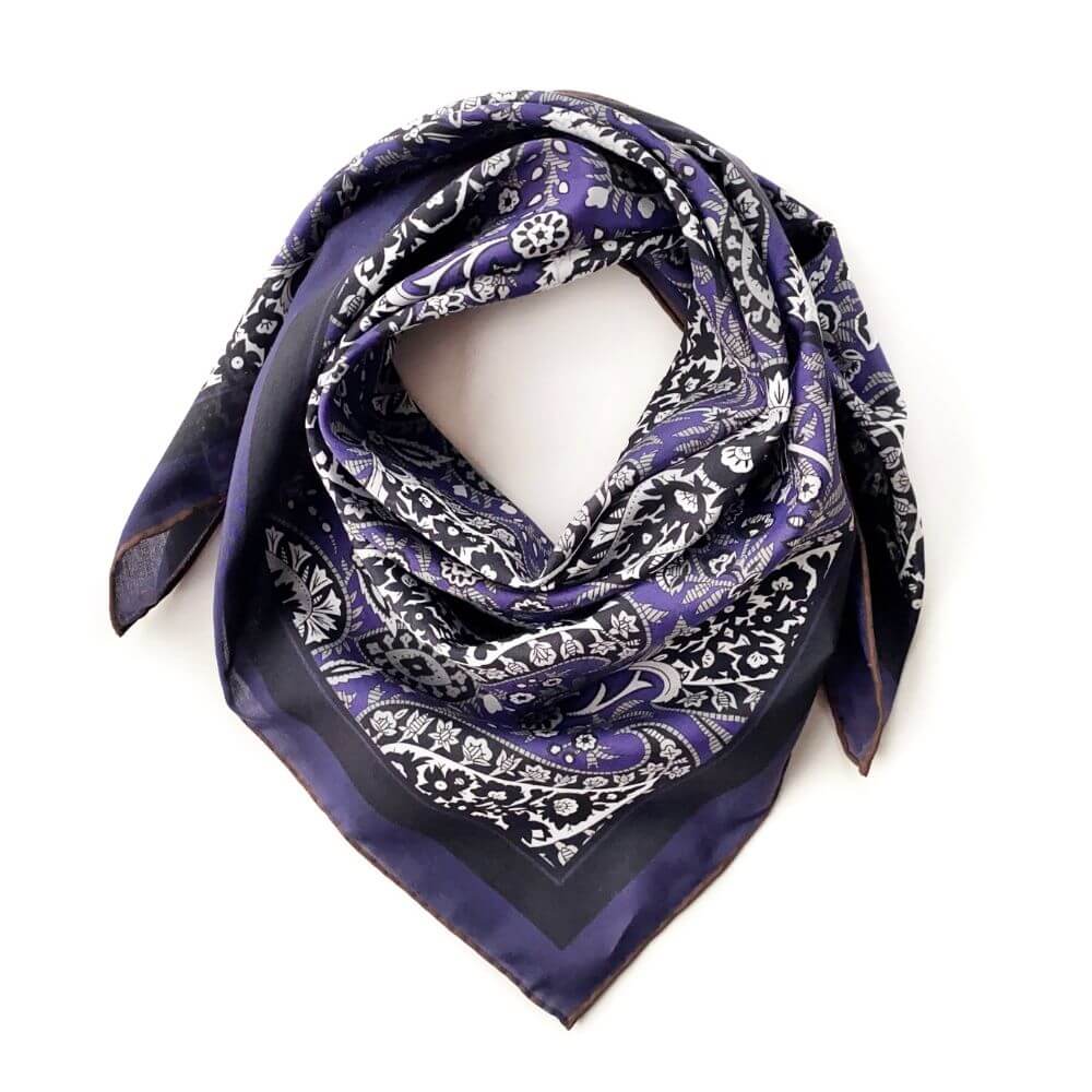 Purple paisley silk cotton blend square scarf folded and shaped into a neckerchief style on a white background.