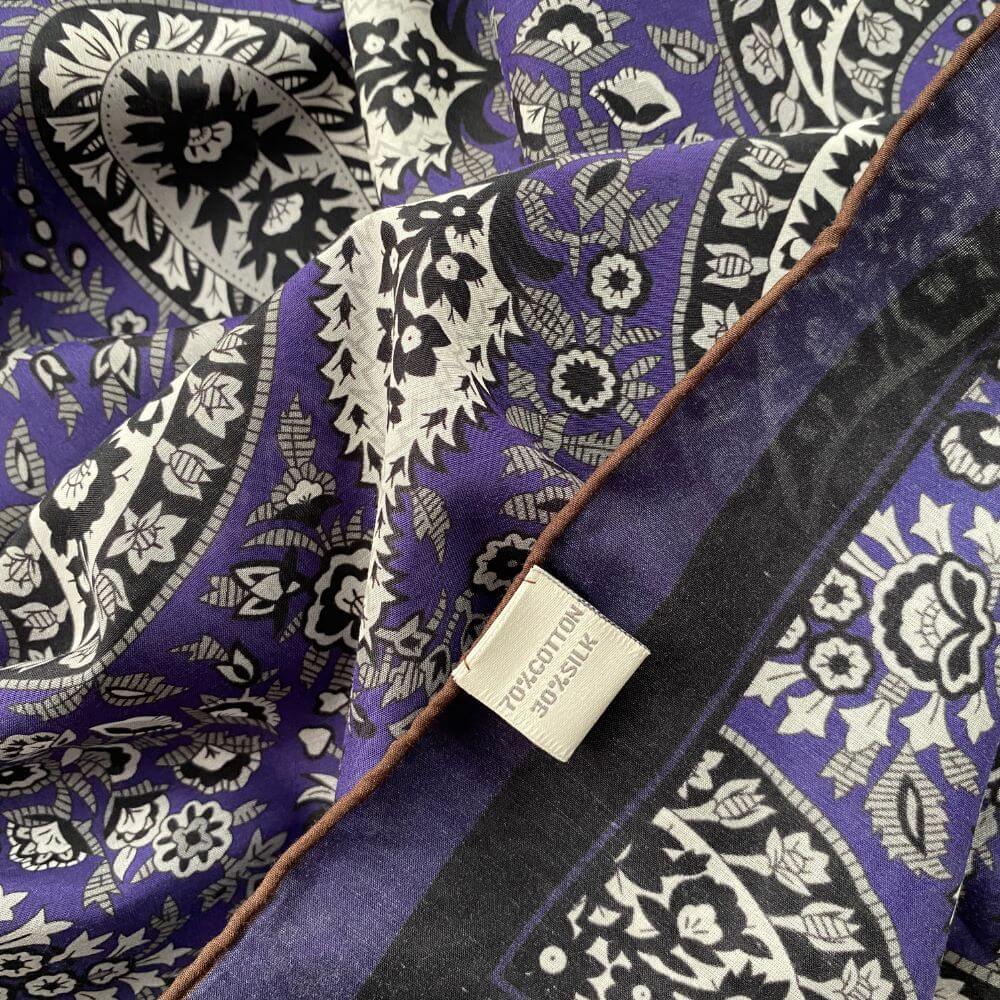 Detail shot of the purple paisley scarf with fabric label showing the 70% cotton and 30% silk blend composition.