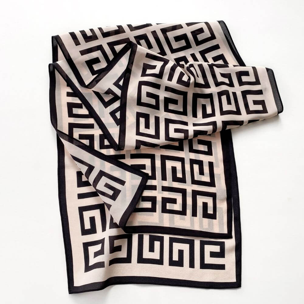 Blush pink and black geometric Mulberry silk scarf laid flat with soft folds, showing the maze-style pattern and border.