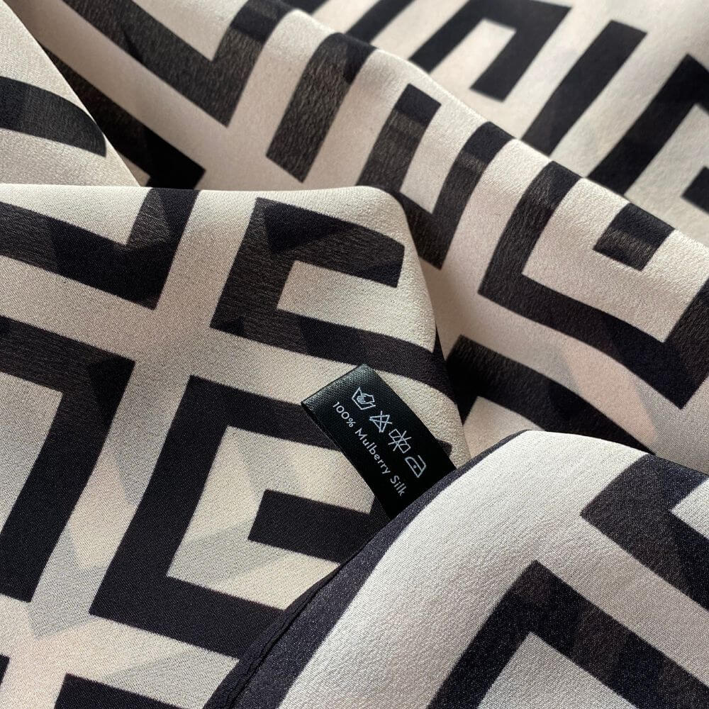 Close-up of the blush pink and black geometric Mulberry silk Crepe de Chine scarf showing the smooth fabric texture and printed pattern.