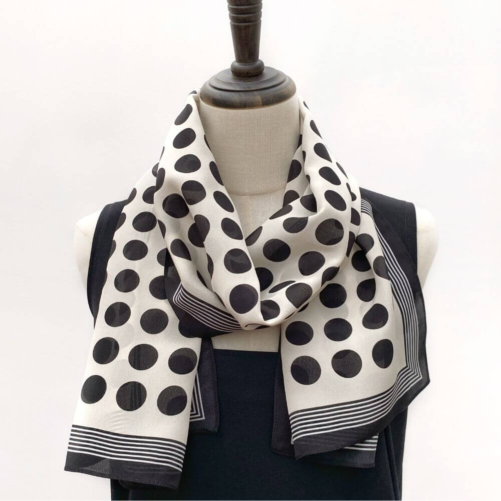 Black and white polka dot silk Crepe de Chine scarf draped around a mannequin, styled loosely around the neck.