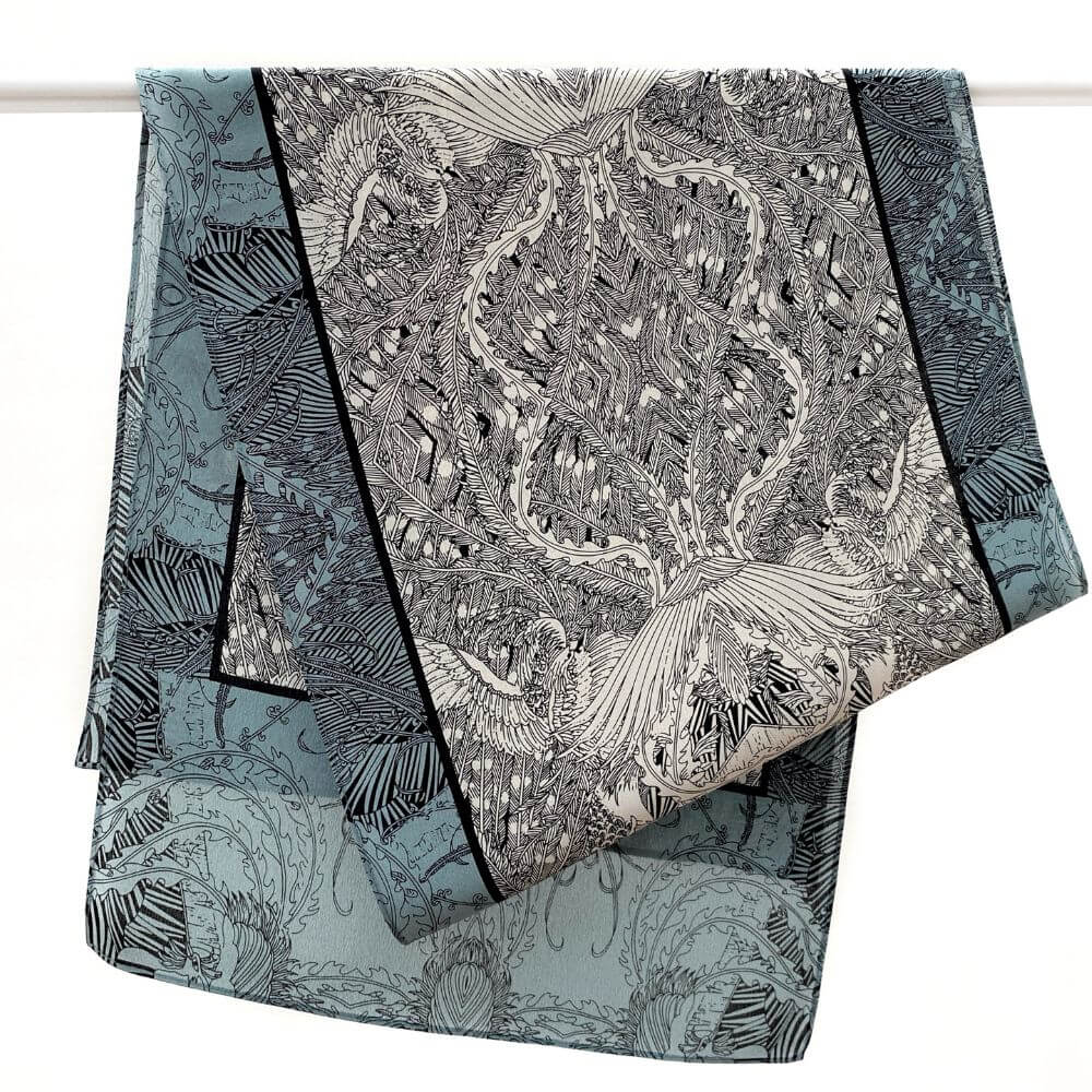 Long blue and black illustrated Mulberry silk Crepe de Chine scarf hanging over a rod, showing the detailed hand-drawn pattern and border.
