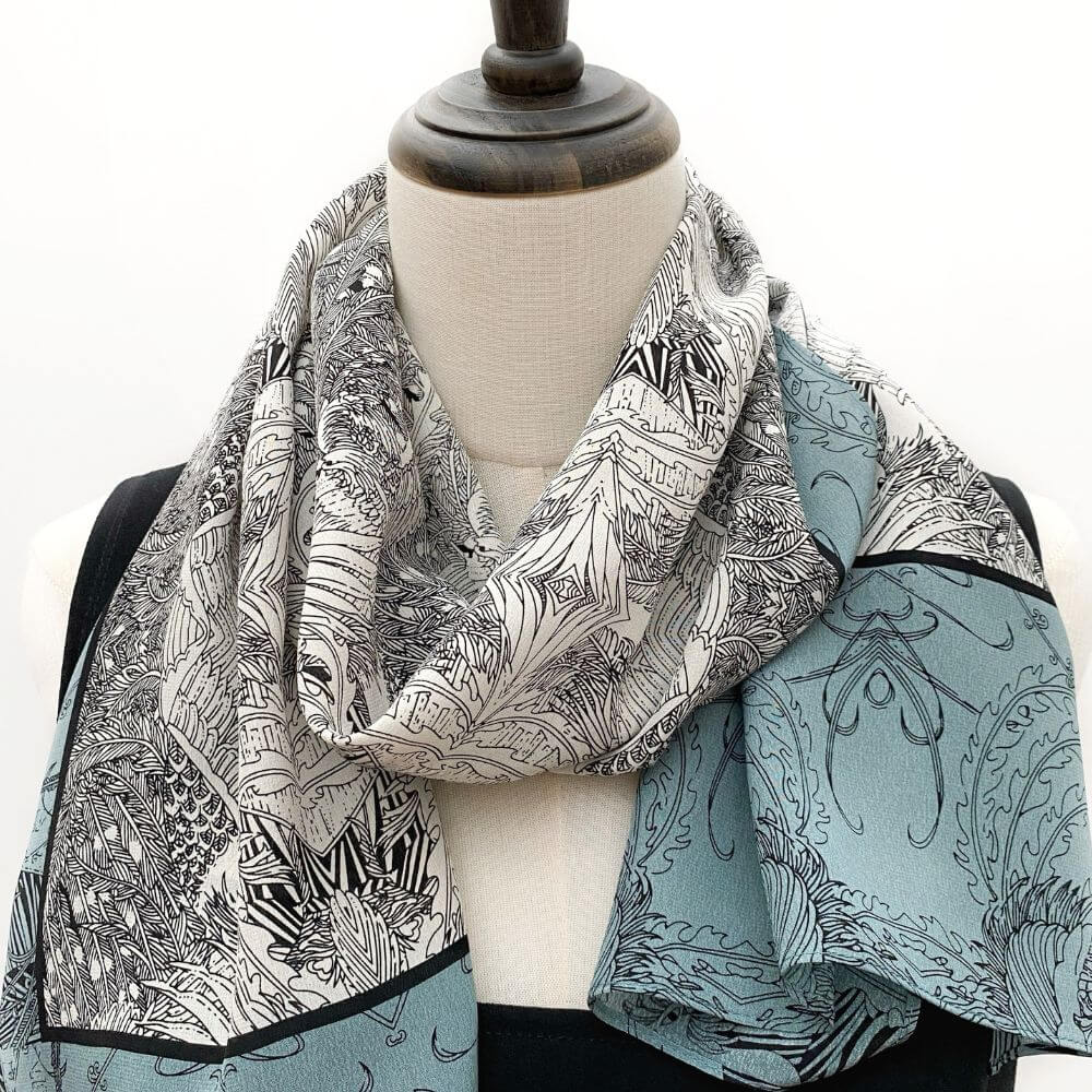 Blue and black illustrated silk Crepe de Chine scarf draped around a mannequin’s neck, showing the intricate linework and soft drape.