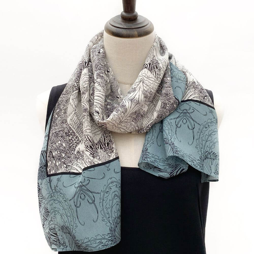 Long blue and black illustrated Mulberry silk scarf styled on a mannequin, displaying the contrasting detailed pattern and smooth fabric texture.