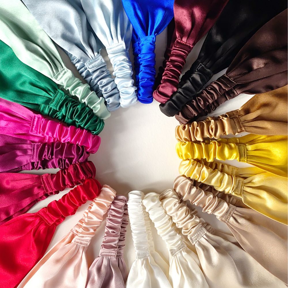 A circular arrangement of silk-flat-headbands in multiple colors, including white, green, blue, burgundy, brown, black, gold, yellow, pink, red, and cream, photographed on a plain light background.
